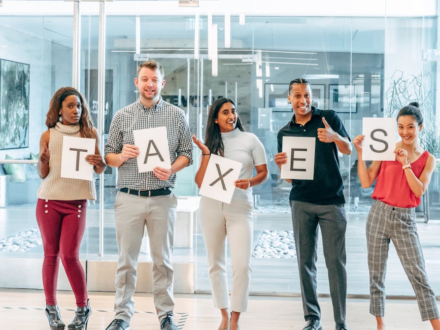 A diverse group of adults holding letters that spell 'taxes' inside an office setting.